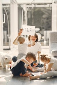 Stressed out mom surrounded by kids holding up a help sign